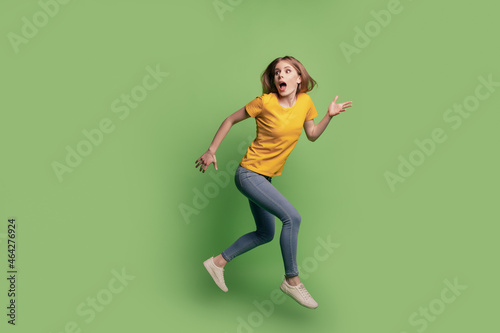 Portrait of crazy curious lady jump run look empty space wear yellow t-shirt jeans sneakers on green background