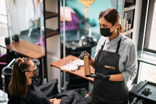 Hairdresser with face mask talks to her customer about hair product in a salon.