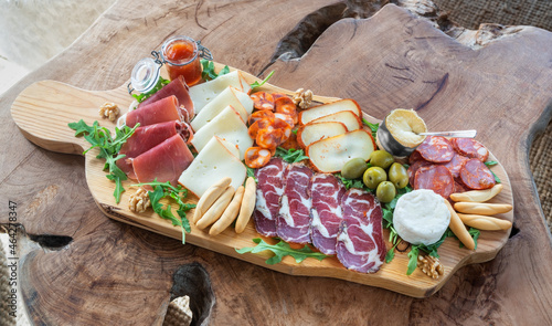 Very colorful tapas board of charcuterie with cheese and smoked meats. Decorated with arugula and walnuts. Wine snacks. On a decorative table.