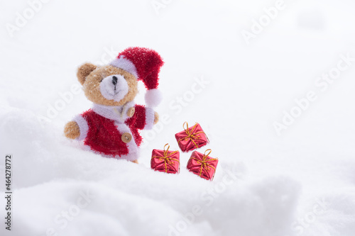 Plush doll dressed as Santa Claus with presents on snowy background. Concept of Christmas with copy space