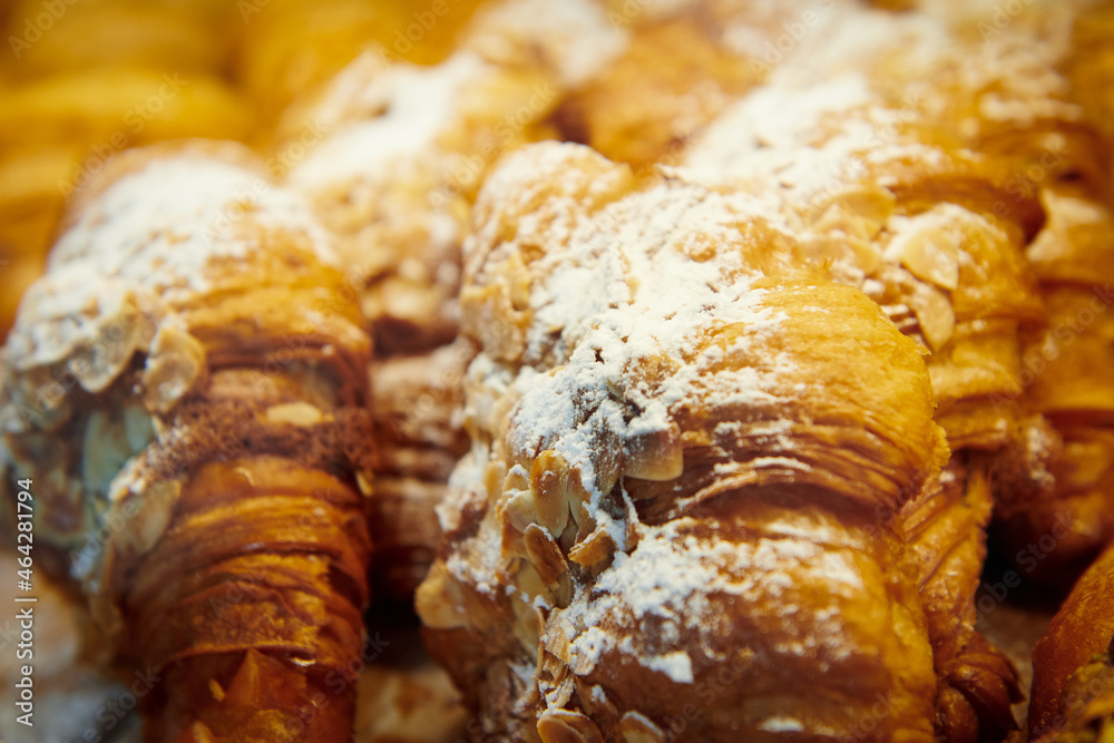 Almond croissants in a pastry shop window. Dessert covered with powdered sugar and almond slices.