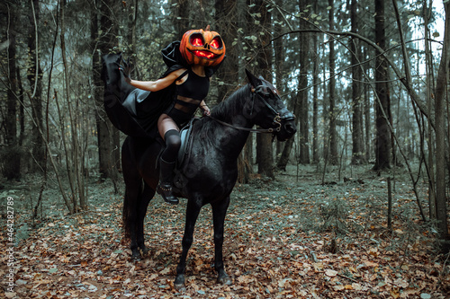the rider is sitting astride a horse. a girl in a long black raincoat with a pumpkin mask with burning eyes. Creepy cosplay shooting for Halloween in the autumn forest. a cloak fluttering in the wind