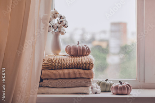 Obraz na płótnie A stack of warm knitted sweaters on the windowsill with pumpkins and a vase of cotton plant in pastel shades w salonie