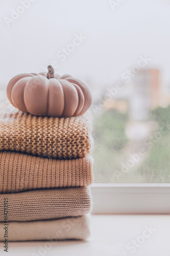 A stack of warm knitted sweaters on the windowsill with pumpkin in pastel shades
