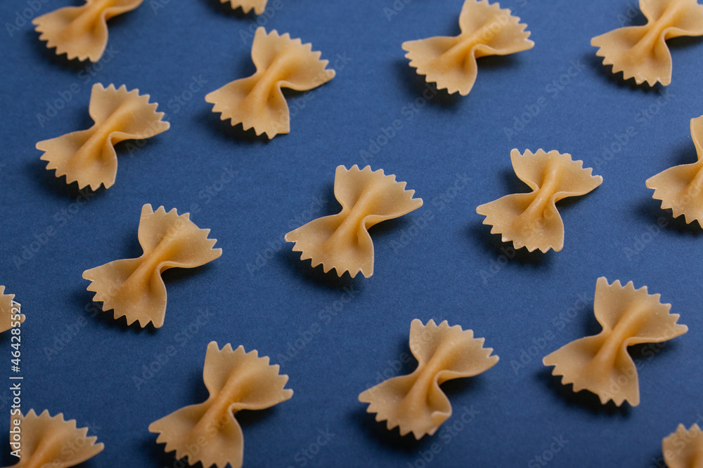 Pattern made of uncooked farfalle pasta on dark navy background. Macaroni background. Top view, flat lay. Pattern made of uncooked farfalle pasta on dark navy background. Macaroni background. Top view, flat lay.