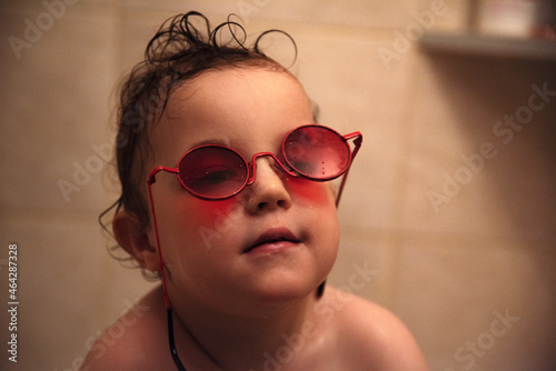 Mały chłopiec w popsutych czerwonych okularach przeciwsłonecznych, siedzący w wannie podczas kąpieli
