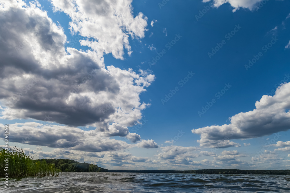 Summer landscape with river, opposite bank and grass and sky with clouds