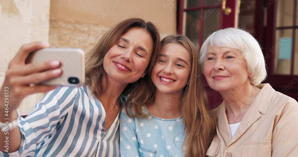 Beautiful caucasian woman sitting with her teenage daughter and mother on terrace of cafe, and taking selfie using smartphone. Beautiful caucasian woman sitting with her teenage daughter and mother on terrace of cafe, and taking selfie using smartphone.