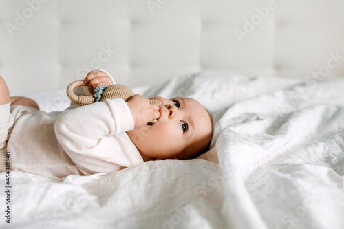 Five months old baby lying on bed, playing with a toy, biting it.