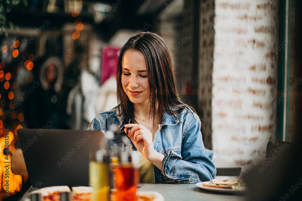 Young female student working on laptop in bar and eating pizza Young female student working on laptop in bar and eating pizza