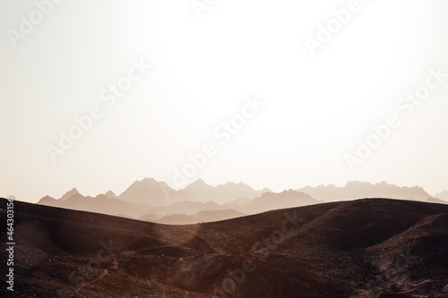 Desert landscape. Stony hills in the foreground with the silhouette of rocky mountains. Sun glare from sunset light. Space, fantastic atmosphere in the sahara desert