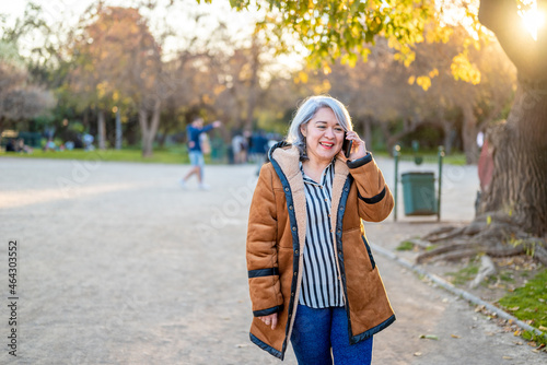 Portrait of a woman with gray hair using the phone at the park at sunset