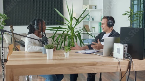 A Male Presenter Communicates with a Guest, an African American, During a Radio Broadcast at a Table in a Recording Studio, Broadcasts a Live Radio Interview With Spbd. Male Host Sharing Content.