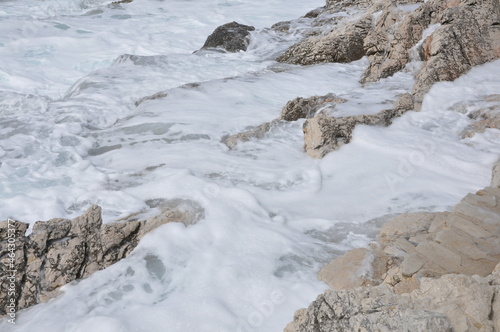 The sea splashing against rocks on a beach. Splashing waves over pebbles in Rijeka, Croatia.Foamy sea water splashing against rocks on the beach closeup