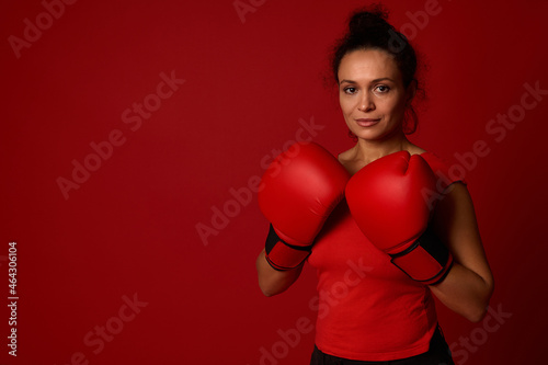 Martial art concept. Middle aged African female athlete, boxer poses with boxing gloves against red background with copy space for advertising for boxing day event photo
