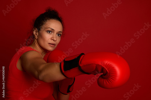 Boxer female athlete fights in red boxing gloves on a red background. Martial art concept with copy space for advertisement for boxing day event photo