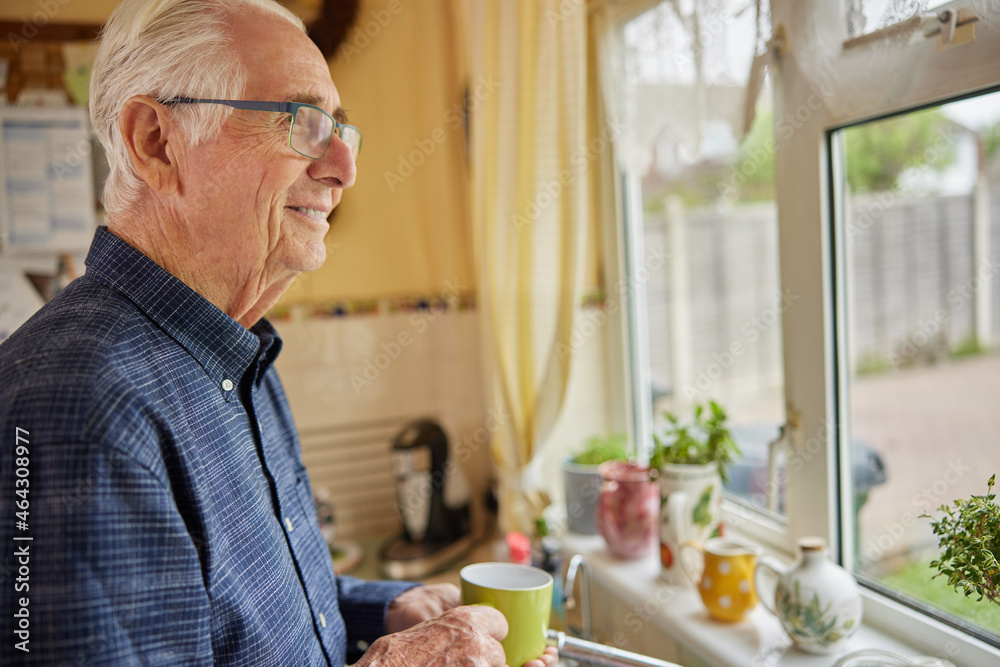 Smiling Senior Man Looking Out Of The Window Holding Cup