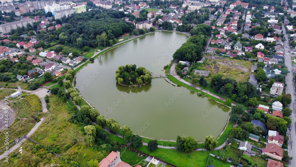 View of the pond in the park in Kolomyia. Island on a city lake. Roofs of residential buildings. Ukraine, Europe