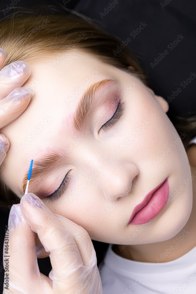 a beautiful blonde in the eyebrow lamination procedure, the master gives shape and combs her eyebrows with a brush a beautiful blonde in the eyebrow lamination procedure, the master gives shape and combs her eyebrows with a brush