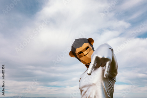Person in geometric monkey mask gesticulating rock n roll against clouds photo
