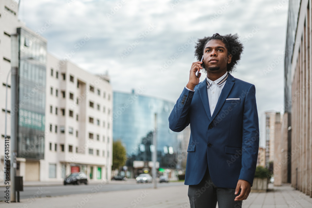 Businessman black ethnicity in blue suit talking on the phone in the street Businessman black ethnicity in blue suit talking on the phone in the street
