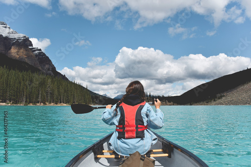 Young girl paddling in a canoe on turquoise lake surrounded by mountains