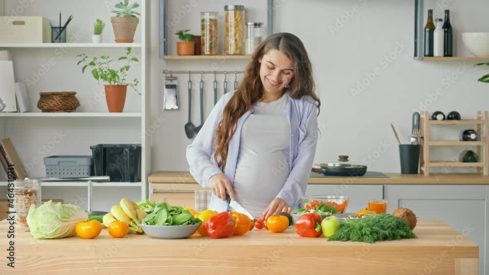 Happy Pregnant Woman Enjoying Preparing a Salad, Cutting Organic Vegetables in Home Kitchen With Modern Interior. Healthy Eating During Pregnancy. A Pregnant Woman Prepares Food at Home. Happy Pregnant Woman Enjoying Preparing a Salad, Cutting Organic Vegetables in Home Kitchen With Modern Interior. Healthy Eating During Pregnancy. A Pregnant Woman Prepares Food at Home.