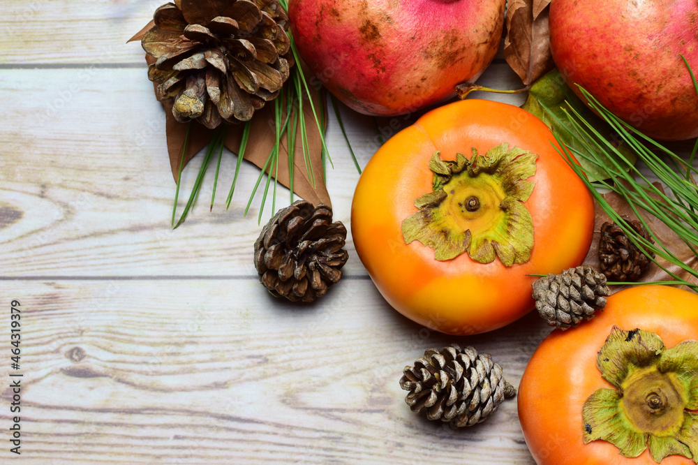 Persimmon and pomegranate on rustic woods, decorated with dried natural leaves and pineapples.