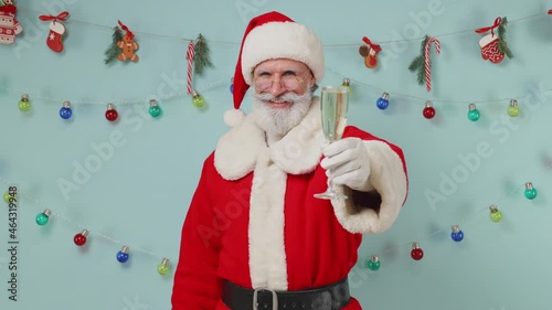 Old bearded Santa Claus man 50s wear Christmas hat suit clothes raise cheer glass of champagne isolated on plain pastel light blue background studio. Happy New Year 2022 merry ho x-mas holiday concept photo