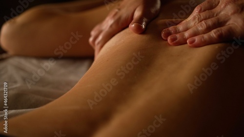 Relaxed young woman having healing body massage. Female therapist rubbing lady's back, giving her relaxing massage. Close-up of the masseuse hands doing back massage. Body care, massage, spa concept. 