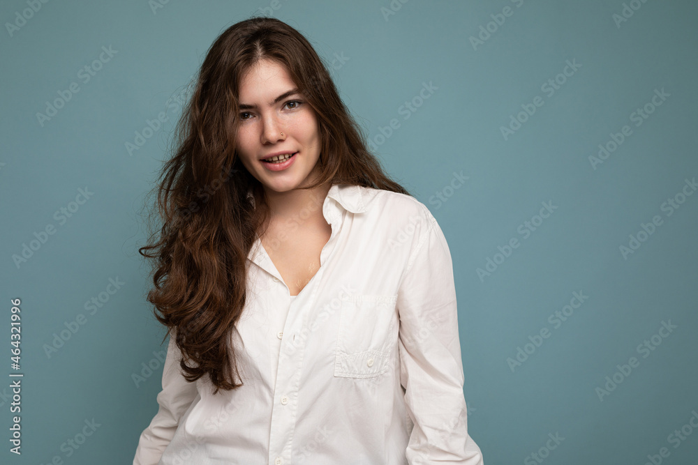 Attractive cute nice adorable tender young curly brunette woman wearing white shirt isolated on blue background with copy space Attractive cute nice adorable tender young curly brunette woman wearing white shirt isolated on blue background with copy space