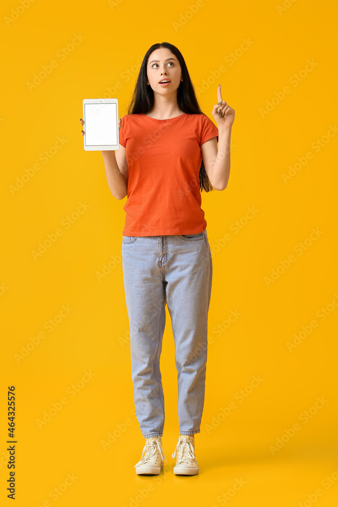 Beautiful teenage girl with tablet computer pointing at something on yellow background Beautiful teenage girl with tablet computer pointing at something on yellow background