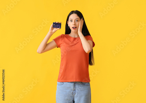 Surprised teenage girl with credit card on yellow background