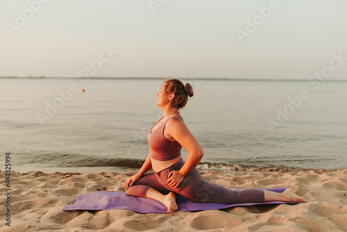 Caucasian woman practicing yoga at seashore sandy beach on sunrise. Womens health and wellness. Sports body positive