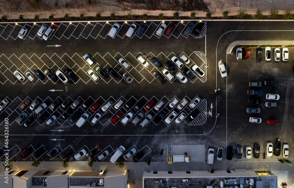 Drone aerial view of parking lots with cars at night. Crowded shopping mall car park.