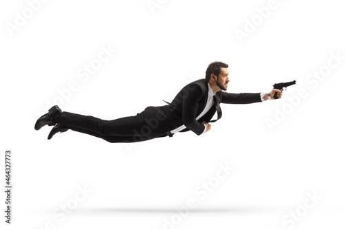 Full length profile shot of a man in a suit flying and holding a gun