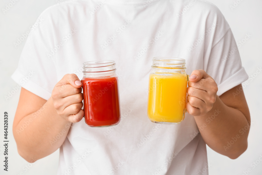 Woman with mason jars of healthy juice on light background