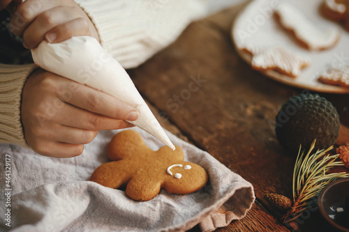 Foto Hands decorating christmas gingerbread man cookie with frosting on rustic table with napkin, spices, decorations