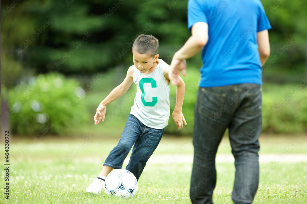 緑の芝生の上で元気よくサッカーをして遊ぶ男の子と父親 緑の芝生の上で元気よくサッカーをして遊ぶ男の子と父親