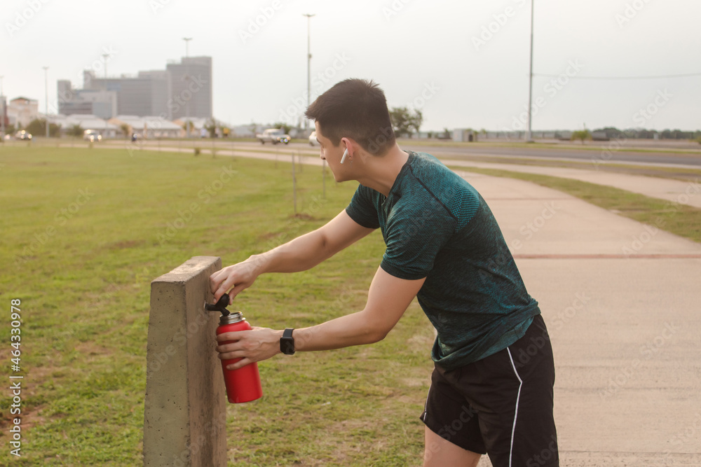 Athletic man carrying water from the public drinking fountain while listening to music on his headphones.