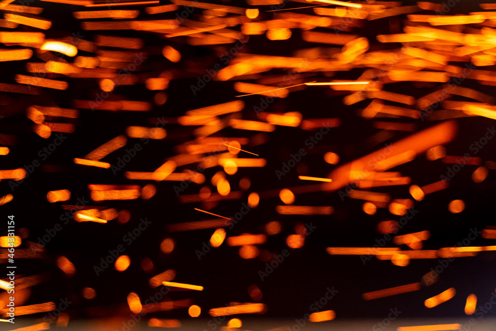 Burning red hot sparks fly from large fire in the night sky. Burning embers glowing flying away particles over black background
