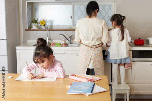 台所で勉強をする小学生の女の子と家事をするお母さん