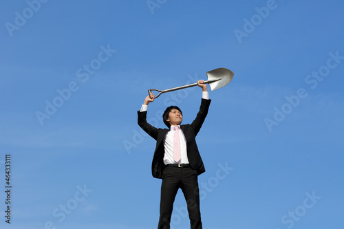 青空の背景でシャベルを天に掲げている笑顔のビジネスマン photo