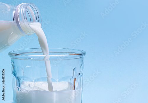 Milk is poured into a glass on a light blue background.