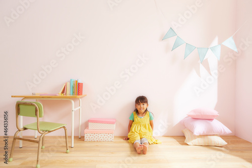 ピンク色の壁の子供部屋で勉強机の横の床に座っている女の子 photo