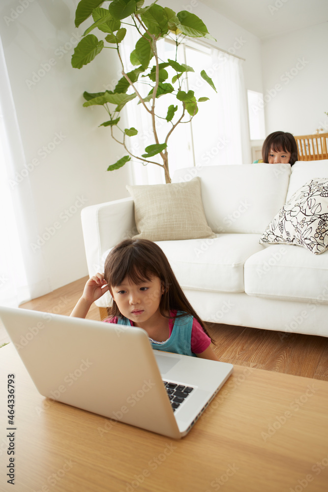リビングテーブルでパソコンを見る女の子とそれを見る兄弟 リビングテーブルでパソコンを見る女の子とそれを見る兄弟