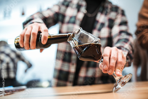 the bartender pours dark beer from a bottle into a glass