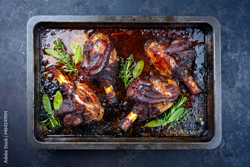Traditional braised slow cooked lamb shank in red wine sauce with herbs served as top view in a barbecue metal sheet