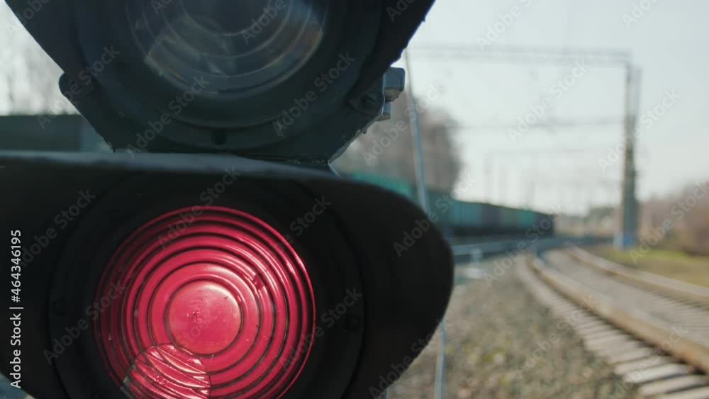 A semaphore with a red signal on a railway stretch. A long freight train passes out of focus in the background. Well-established operation of all systems on the railway.