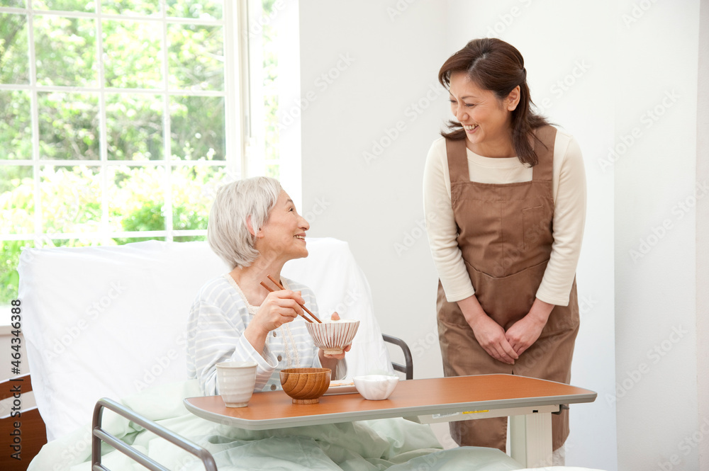 介護ベッドのシニア女性に食事の世話をする介護ヘルパー
